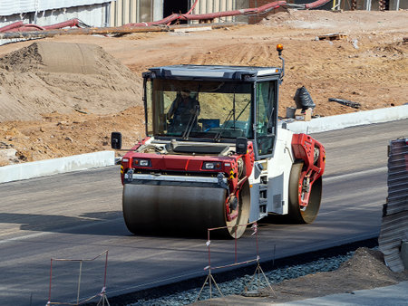 A road roller drives along a new asphalt road. Industrial background with road roller on a...