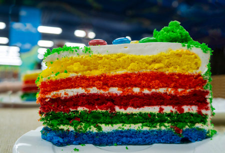 A piece of beautiful delicious cake lies on a plate. Rainbow sponge layers alternate with cream....
