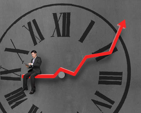 Businessman using tablet and sitting on growth red arrow with clock face in concrete wall background