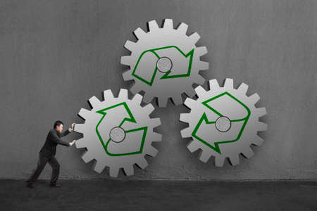 Businessman rolling 3 large concrete gears with recycle mark in concrete wall background.の写真素材