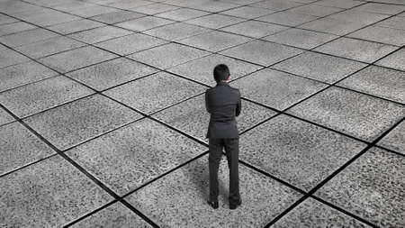 Rear view businessman thinking and standing on endless tiled floor with hands crossed on his chestの写真素材