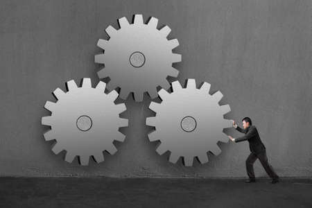 Businessman rolling 3 large concrete gears in concrete wall background の写真素材