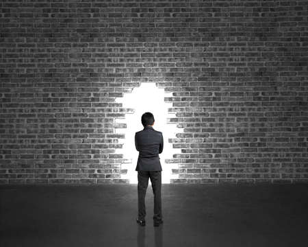 Businessman stand opposite to big hole on bricks wall in dark place with concrete floorの写真素材
