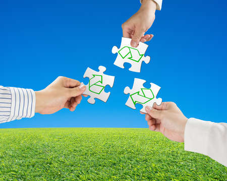 Hands hold puzzles with recycle symbol and beautiful landscape green meadow, clear blue sky...