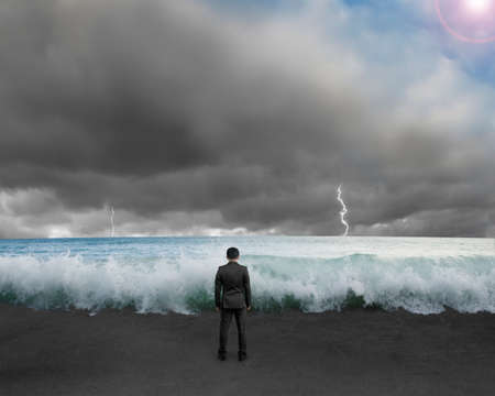 Businessman standing toward waves and cludy sky with Lightning , thunder to challenge dangerous situationの写真素材