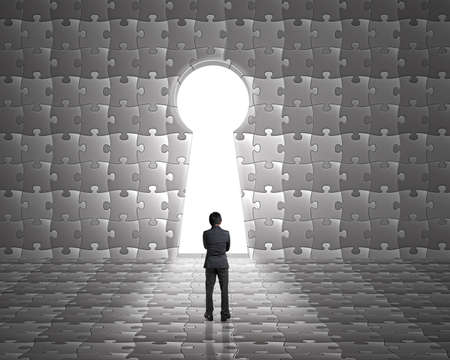 Businessman stand toward key hole shape door on puzzles wall with bright outside backgroundの写真素材
