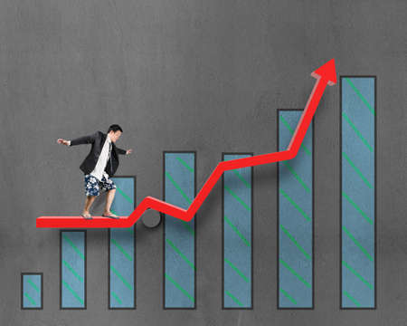 Businessnan surfing on growth red arrow with histogram drawing on concrete wall backgroundの写真素材
