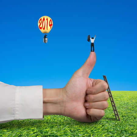 Businessman standing on top of thumb, another in lamp balloon with 2014, meadow and blue sky backgroundの写真素材