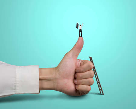 Businessman standing on top of thumb with 2 hands up, green backgroundの写真素材