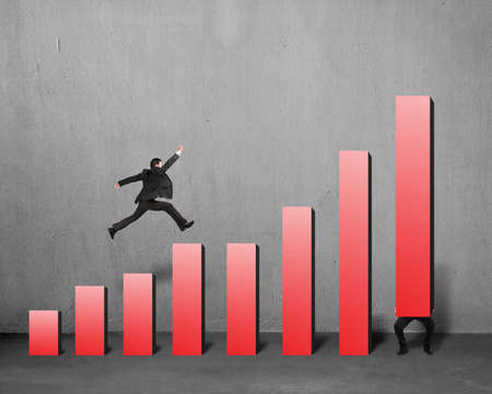 Businessman running and jumping on red bar chart with another lift one in concrete backgroundの写真素材