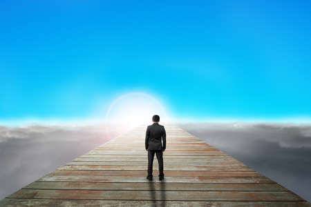 businessman standing on wooden path looking sunrise with cloudy below and blue sky