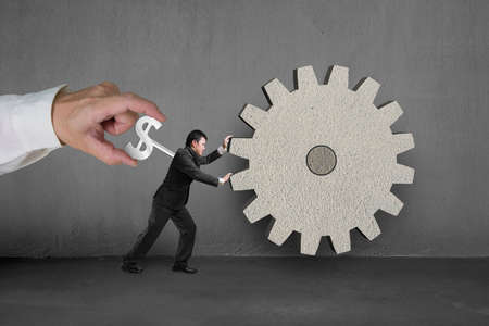 Hand winding winder on businessman to work on large concrete gearの写真素材