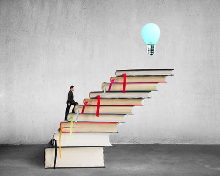 Businessman climbing on stack of books with growing bulb in concreteの写真素材