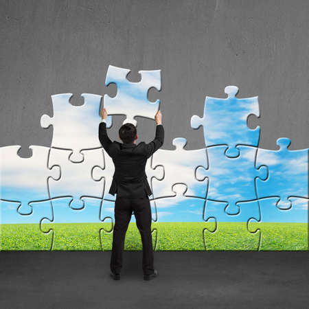 Businessman holding puzzles to assembly for changing view on concrete wallの写真素材