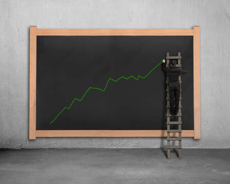 Businessman on ladder drawing growing green arrow trend on black boardの写真素材