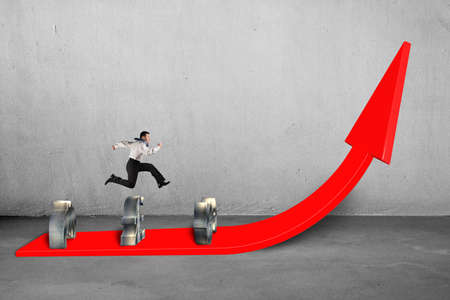 Businessman jumping over money symbols on growing red arrow with concrete の写真素材