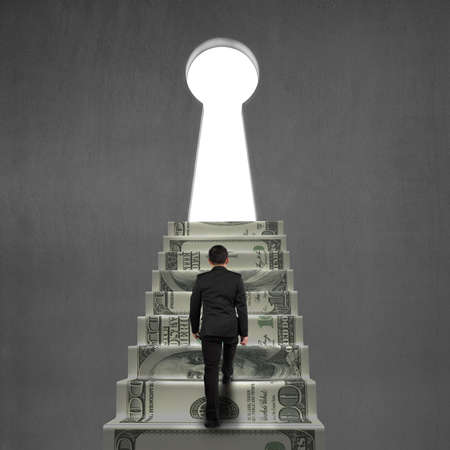 Climbing on money stairs to key hole on concrete wallの写真素材
