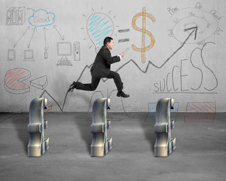 Jumping over pound with business doodles on concrete wallの写真素材
