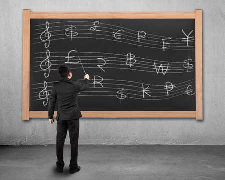 Businessman conducting and facing stave with money symbols on blackboardの写真素材