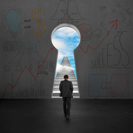 Rear view businessman walking toward key shape hole with stairs and blue skyの写真素材