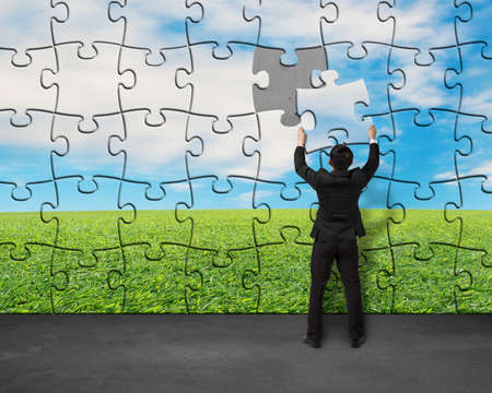 Businessman assembling last missing puzzle on wall for landscapeの写真素材