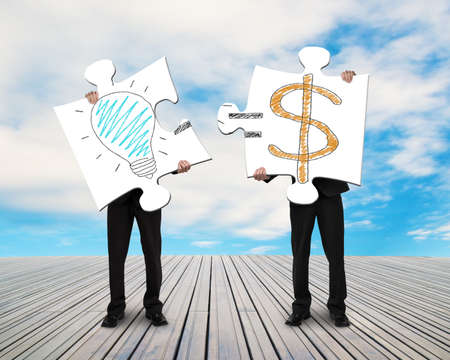 Two businessmen assembling puzzles for Idea is Money doodles blue sky の写真素材