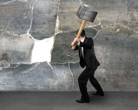 Businessman holding sedgehammer to crack concret wallの写真素材