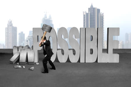 businessman hold sledgehammer to smash impossible 3D concrete word on cement floor and city skyscraper backgroundの写真素材
