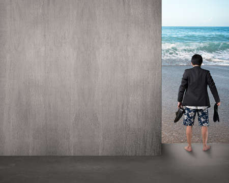 barefoot man hold leather shoes stand on beach entrance with empty concrete wallの写真素材