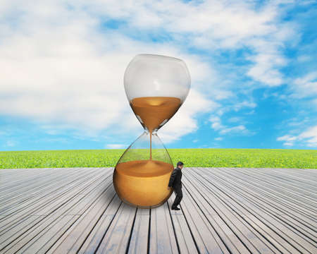 businessman hand keeping inclined hourglass on wooden floor with nature sky 