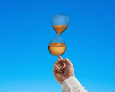 forefinger balancing hourglass isolated on blueの写真素材