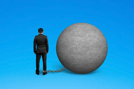 man being trapped with concrete ball isolated on blueの写真素材