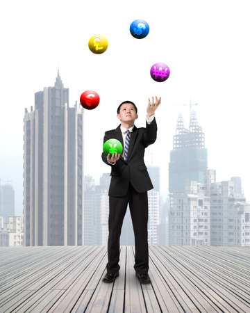businessman throwing and catching currency symbol balls on wooden floor with cityscape backgroundの写真素材