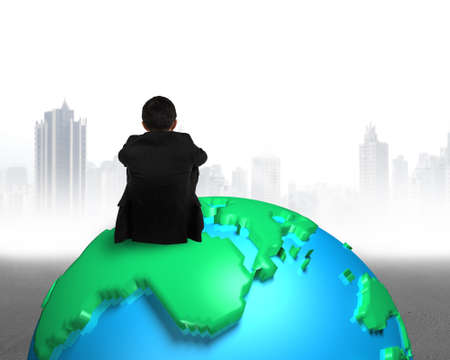 businessman sitting on 3d map globe watching gray buildings cityscapeの写真素材
