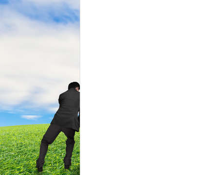 man pushing away white empty wall with nature sky clouds grassの写真素材