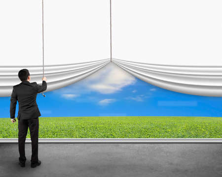 businessman pulling open white blank curtain discovered natural sky meadow on concrete floorの写真素材