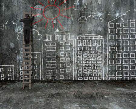 businessman drawing red sun on old mottled concrete wall with city buildings doodlesの写真素材