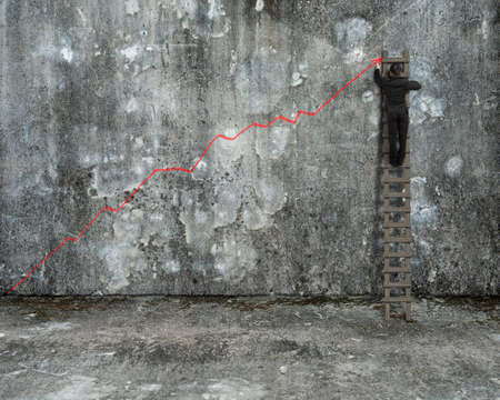 businessman climbing on ladder drawing red growth trend line on old mottled concrete wall and floor backgroundの写真素材