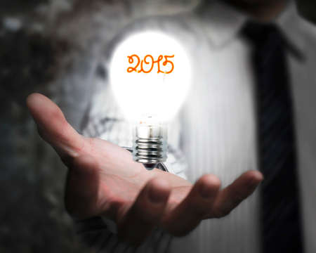 businessman hand holding 2015 light bulb illuminated dark backgroundの写真素材