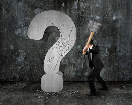 businessman holding hammer cracked question mark with gray mottled concrete wall backgroundの写真素材