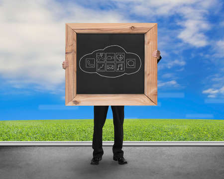 Man holding blackboard with hand-drawn cloud app icons on concrete floor and natural sky grass backgroundの写真素材