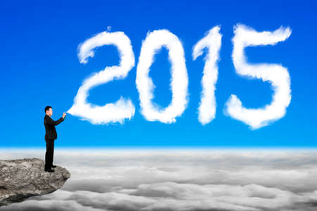 Businessman spraying white 2015 year cloud shape in blue sky cloudscape background