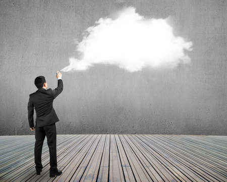 Businessman spraying white cloud paint on gray concrete wall backgroundの写真素材