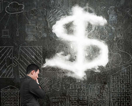 Businessman thinking about dollar sign shape cloud with business concept doodles wall backgroundの写真素材