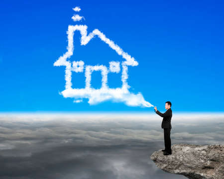 Businessman spraying house shape cloud paint on the cliff with cloudscape backgroundの写真素材
