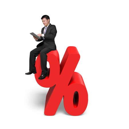 Using tablet businessman sitting on red percentage sign with white backgroundの写真素材
