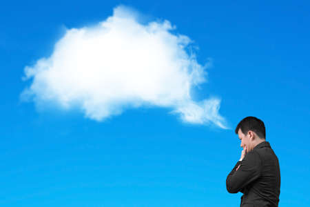 Businessman thinking about white cloud thought bubble above his head isolated on blue backgroundの写真素材