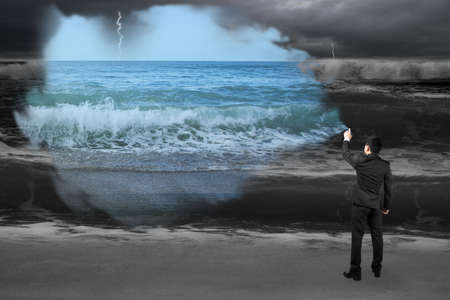Businessman spraying calm sea paint covered dark stormy ocean backgroundの写真素材