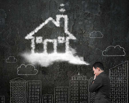 Businessman thinking about house shape cloud with business concept doodles wall backgroundの写真素材