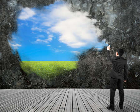 Businessman spraying sky cloud grass paint on dirty concrete wall backgroundの写真素材